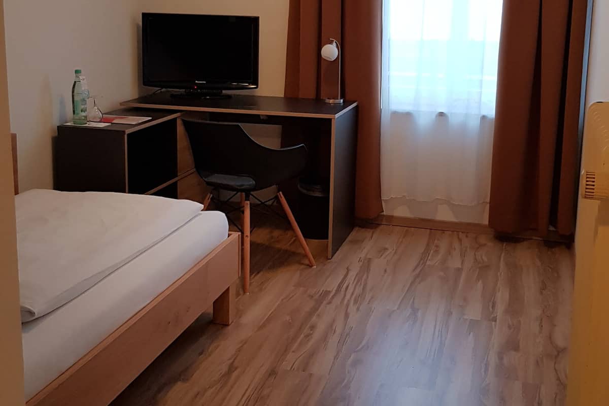 Une chambre d’hôtel avec un lit, un bureau avec un ordinateur, une chaise, une télévision et une fenêtre avec des rideaux.
