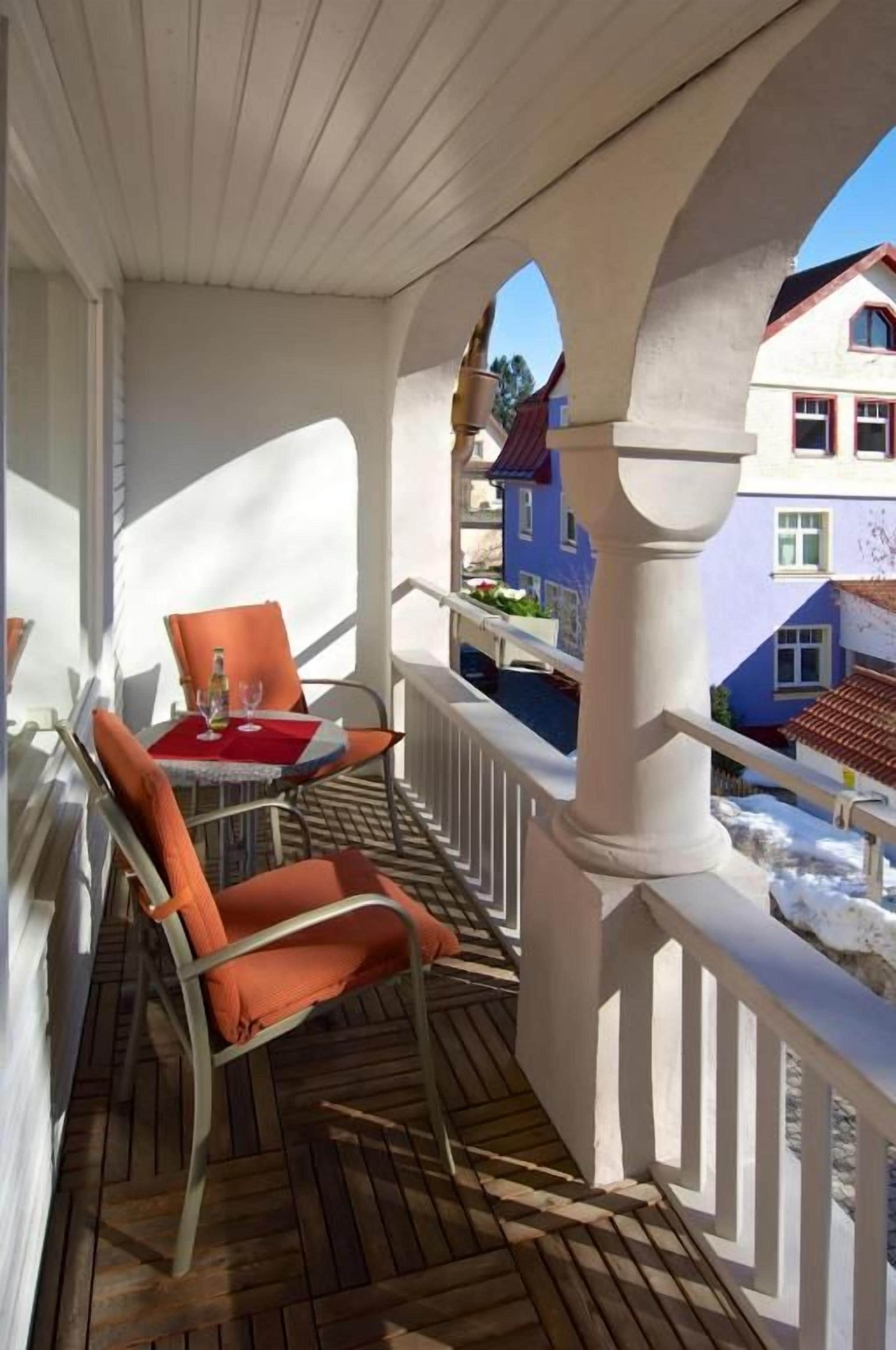 A wooden deck with a white railing, a table with a red tablecloth, and orange chairs.