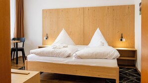 Una cama individual con cabecera de madera, un escritorio, una silla y una alfombra con estampado blanco y negro.