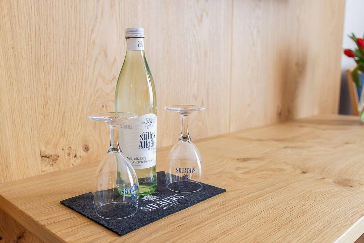 Une bouteille de vin Stilles Allgaur posée sur une surface en bois, avec deux verres à vin à côté.