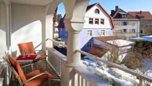 Un balcón con mesa y sillas, con vista a una calle nevada con casas coloridas.