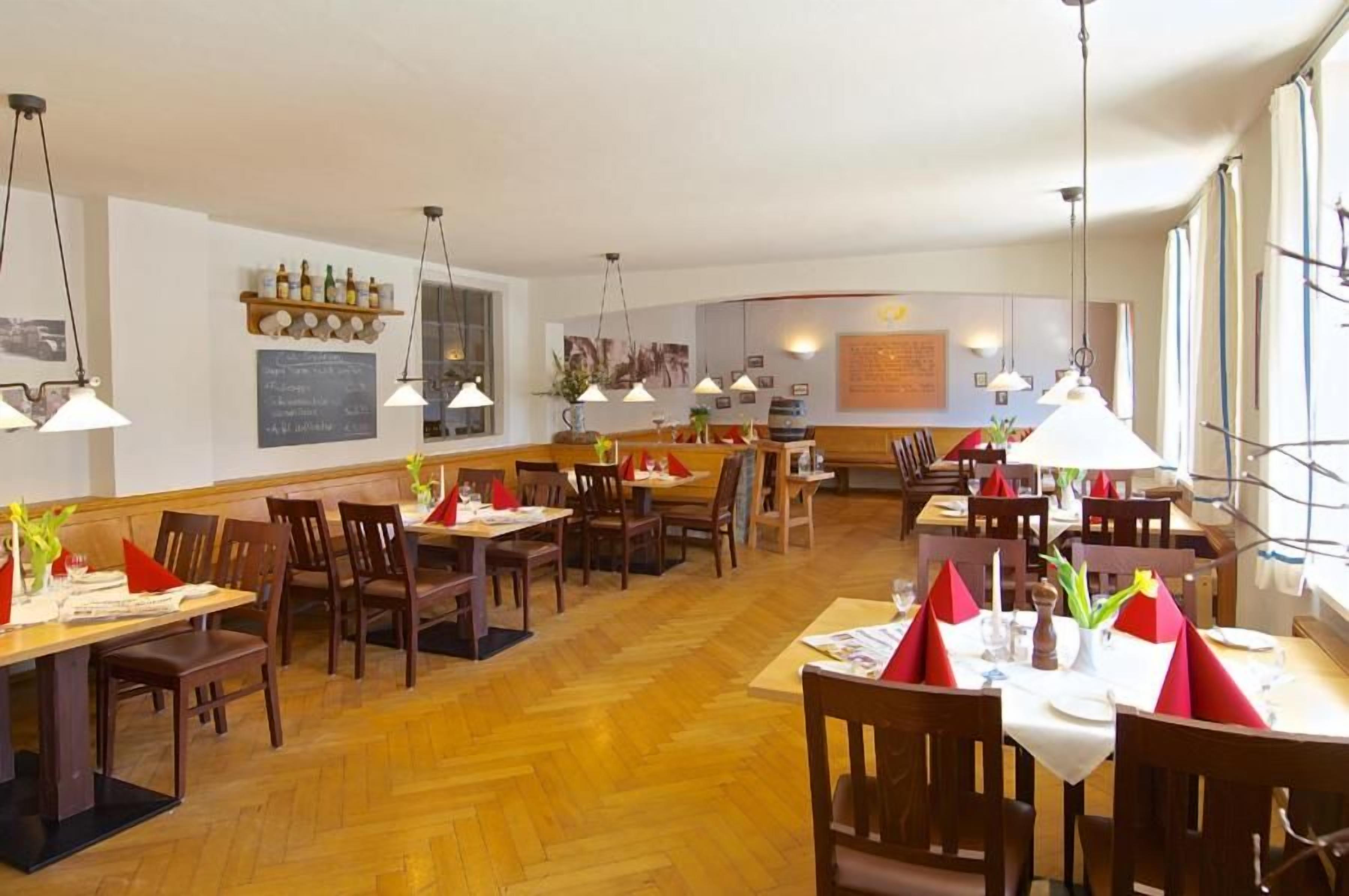 Un restaurante con varias mesas y sillas, suelo de madera, iluminación colgante y una barra de fondo.