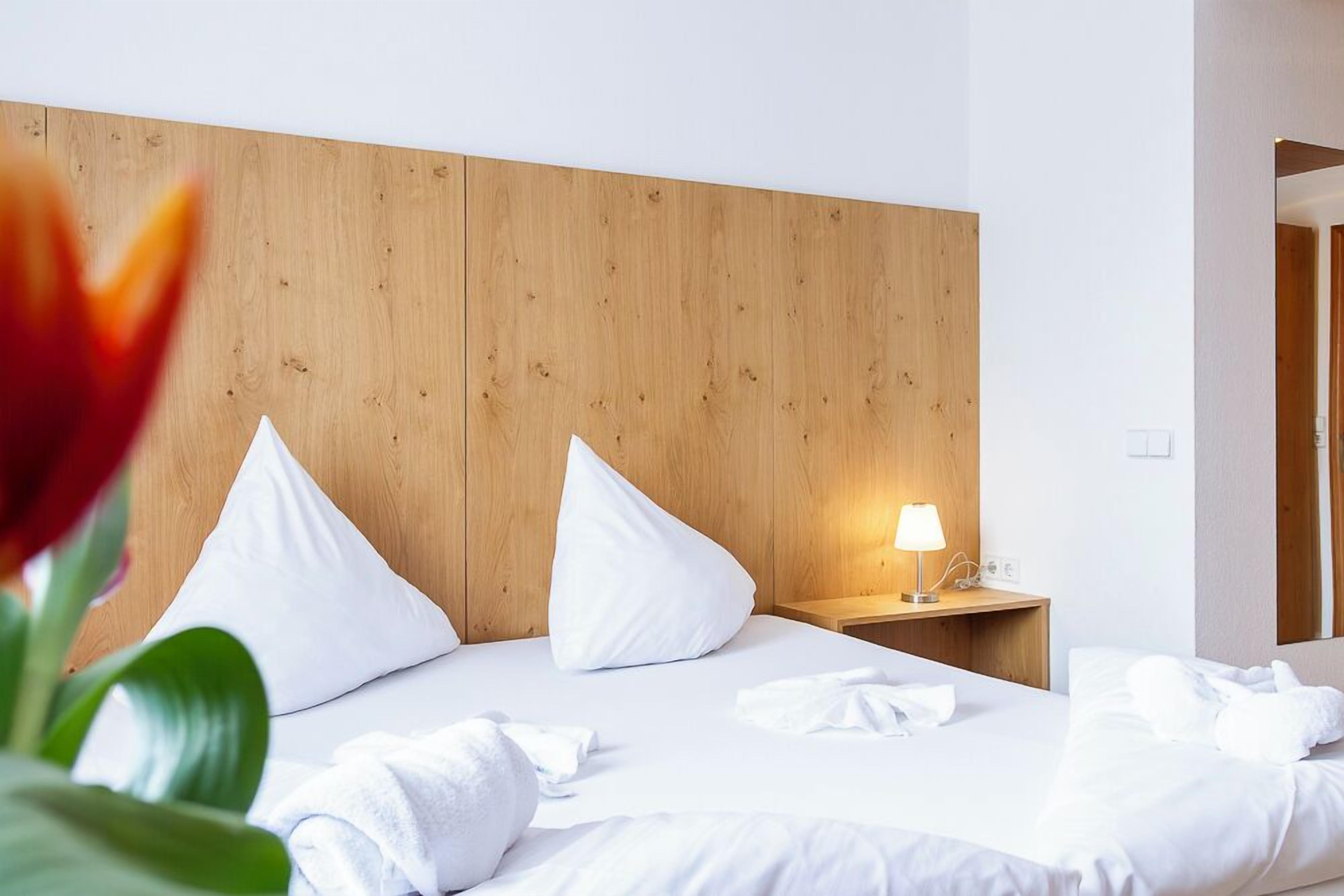 Ein Hotelzimmer mit einem hölzernen Kopfende, einem Nachttisch mit Lampe und ordentlich drapierten Handtüchern.