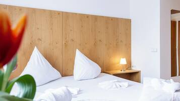 Ein Hotelzimmer mit einem hölzernen Kopfende, einem Nachttisch mit Lampe und ordentlich drapierten Handtüchern.