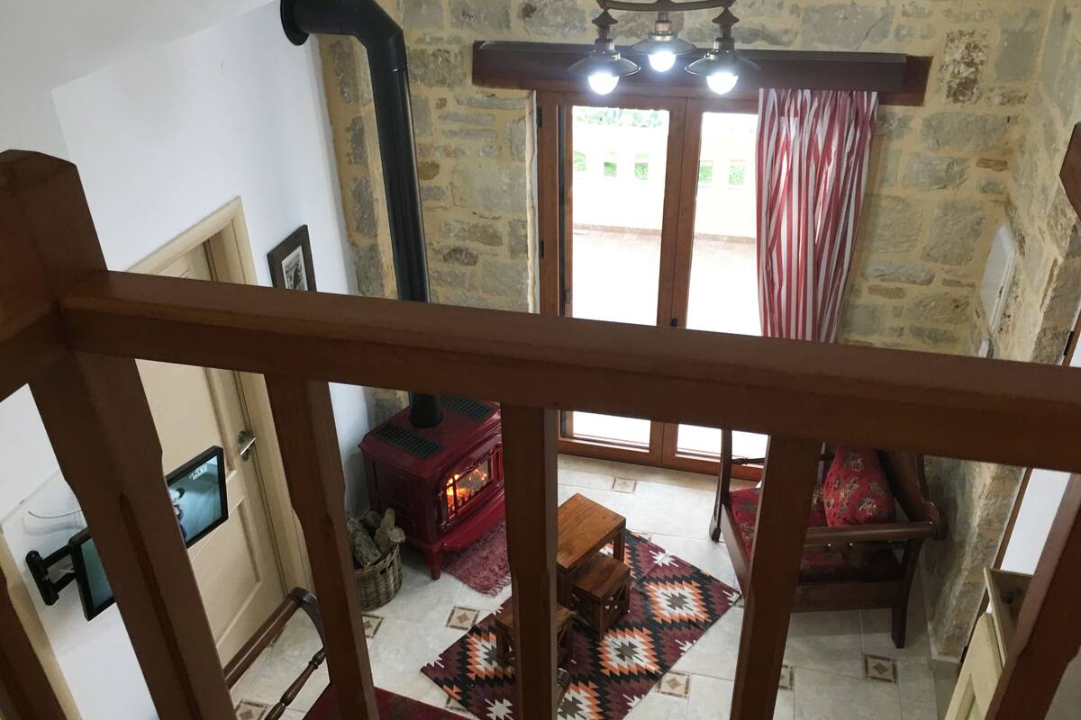 A room with a stone wall, a red wood-burning stove, a wooden bench, and a patterned rug.