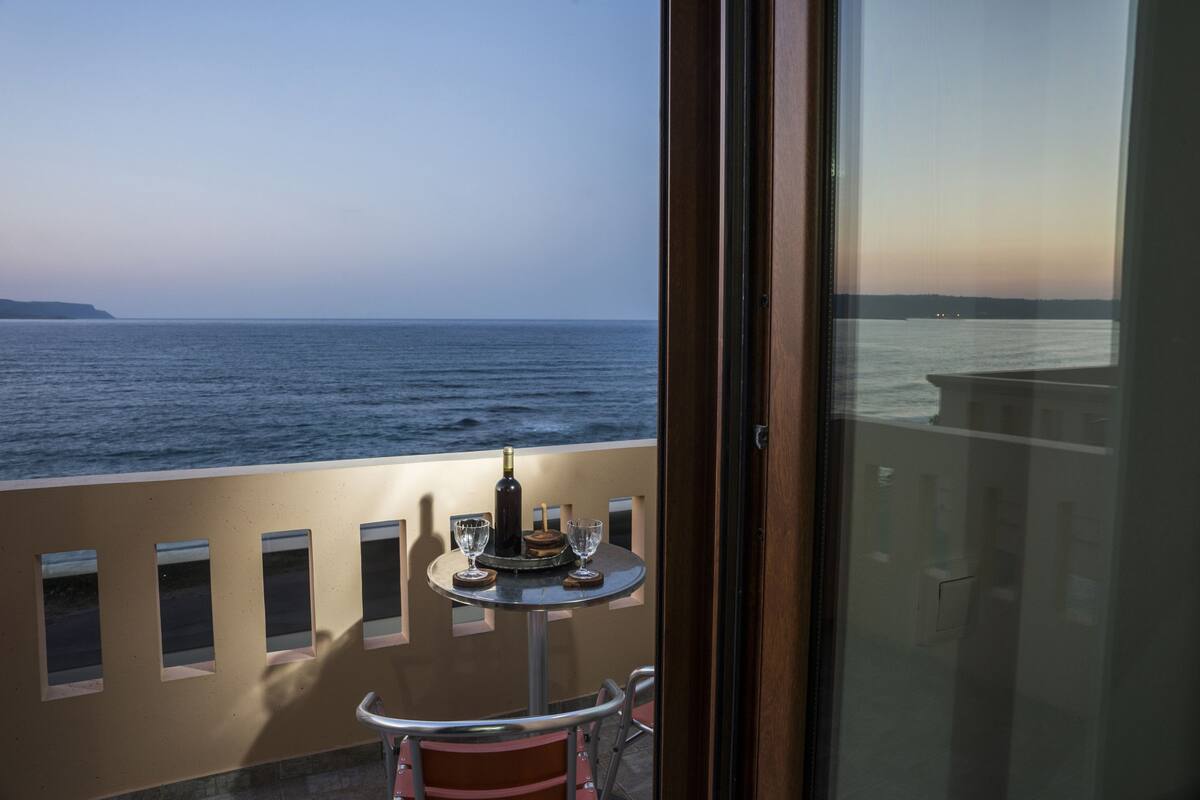 A balcony with a table set for two, overlooking a body of water.