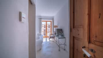 Un couloir avec une porte en bois, un lit, un bureau avec une lampe et une fenêtre donnant sur des immeubles.