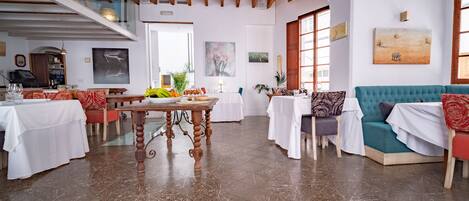 Una habitación amplia con techo alto, vigas de madera, zona de comedor con mesas y sillas, un sofá y obras de arte en las paredes.