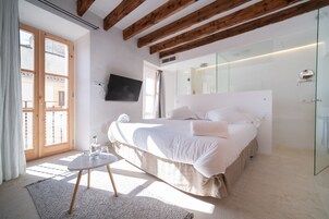 A bedroom with a large bed, a TV mounted on the wall, and a window with curtains.