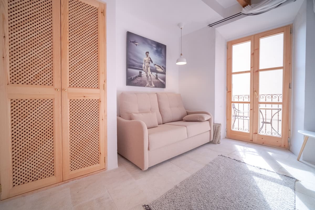 Ein modernes Wohnzimmer mit einem beige farbenen Sofa, Holzklappläden, einem großen Fenster mit Aussicht und einem Gemälde an der Wand.