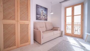 Una sala de estar moderna con un sofá color beige, puertas de madera con listones, un ventanal con vistas y un cuadro en la pared.