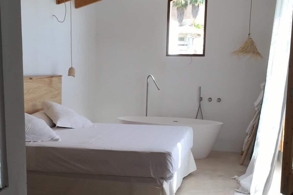 Ein Schlafzimmer mit Bett, ein Badezimmer mit Badewanne und einem Fenster für natürliches Licht.