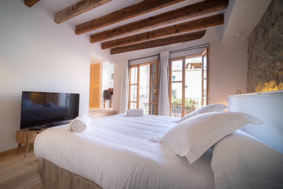 Ein Schlafzimmer mit einem großen Bett, einem Flachbildfernseher, Holzbalken, einem Balkon und einer Steinwand.