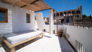Un balcó amb un llit, parets blanques, un sostre de fusta i vista d'un edifici històric amb arcs.