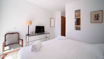 Una habitación de hotel con una cama, un escritorio con televisor, una silla y un cuadro en la pared.