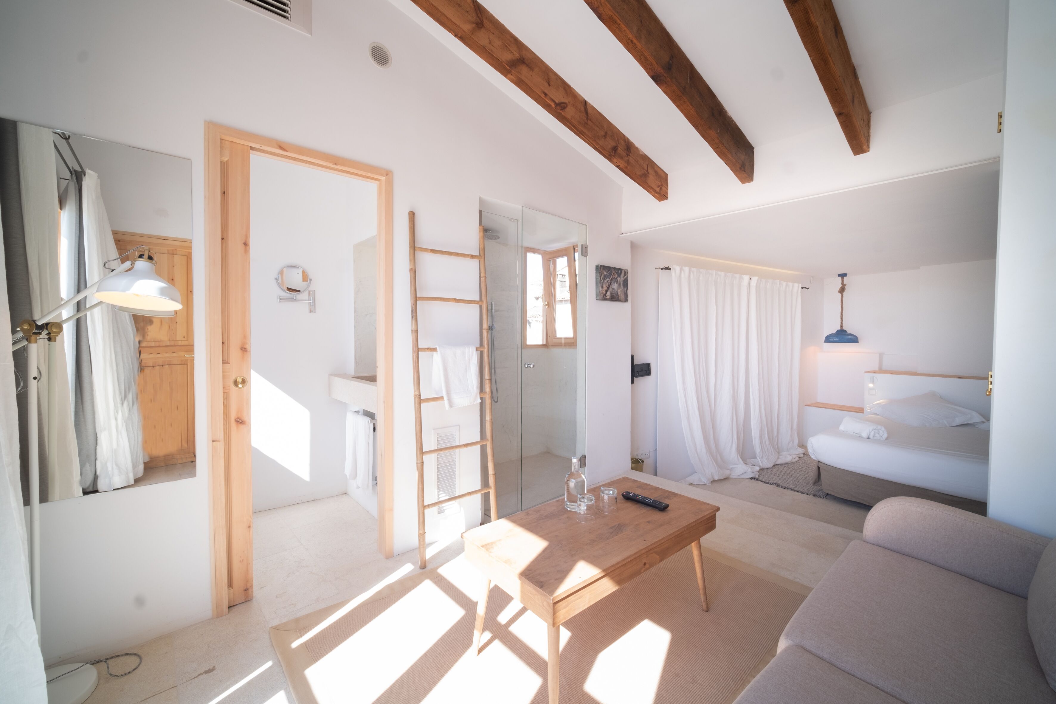 A well-lit room with a wooden ceiling, a sofa, a table with a remote control, and a mirror on the wall.