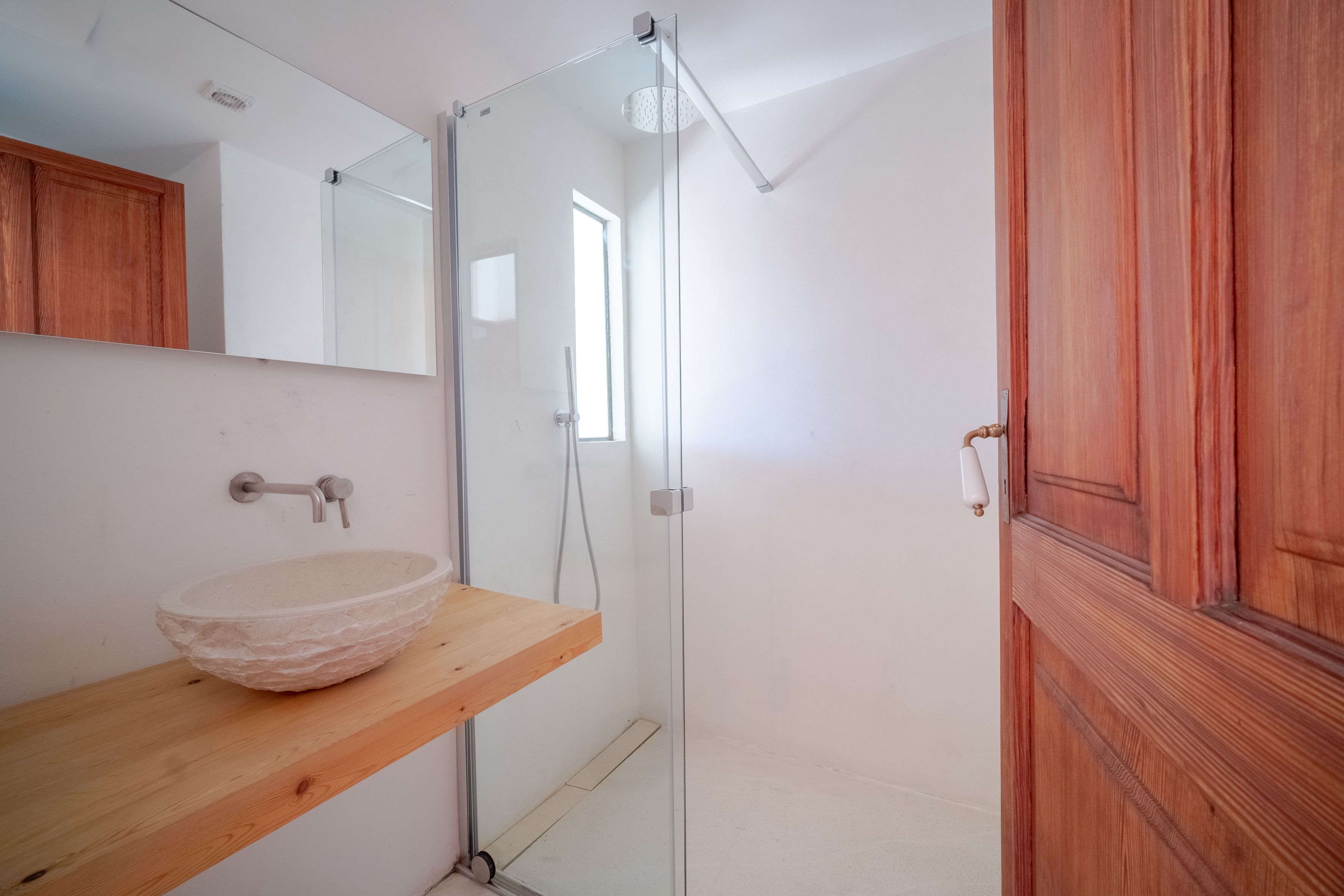 Un baño con tocador de madera, cabina de ducha de vidrio y puerta de madera.