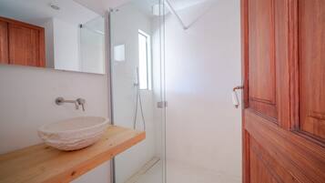 Un baño con tocador de madera, cabina de ducha de vidrio y puerta de madera.