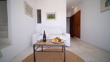 Un salón con un sofá blanco, una mesa de centro con una botella y vasos, y un frutero.