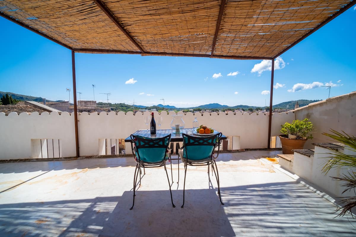 Eine Terrasse im Freien mit Tisch und Stühlen, einem Blumentopf und Blick auf ferne Hügel.