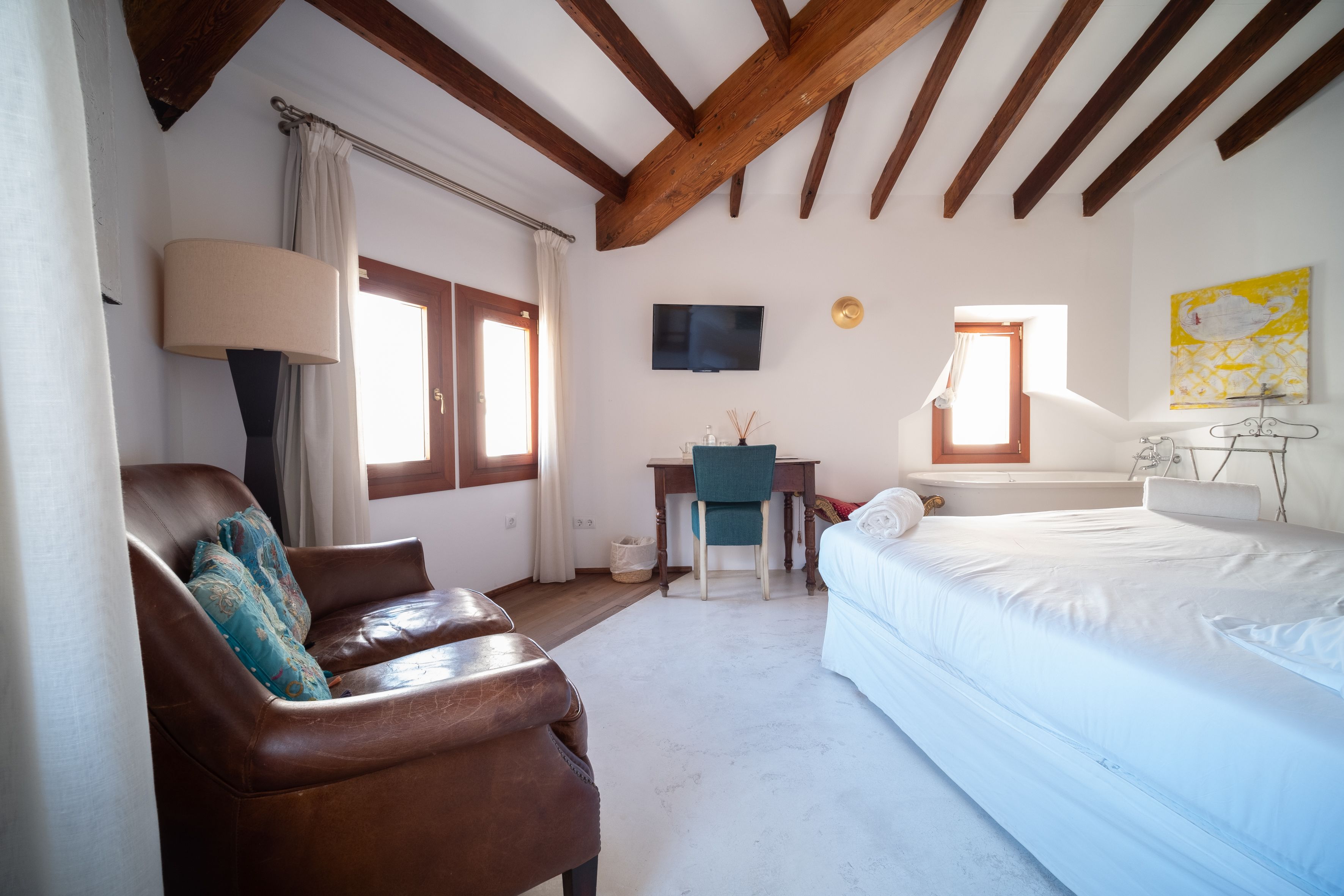 A bedroom with a bed, a desk, a chair, a sofa, and a TV.