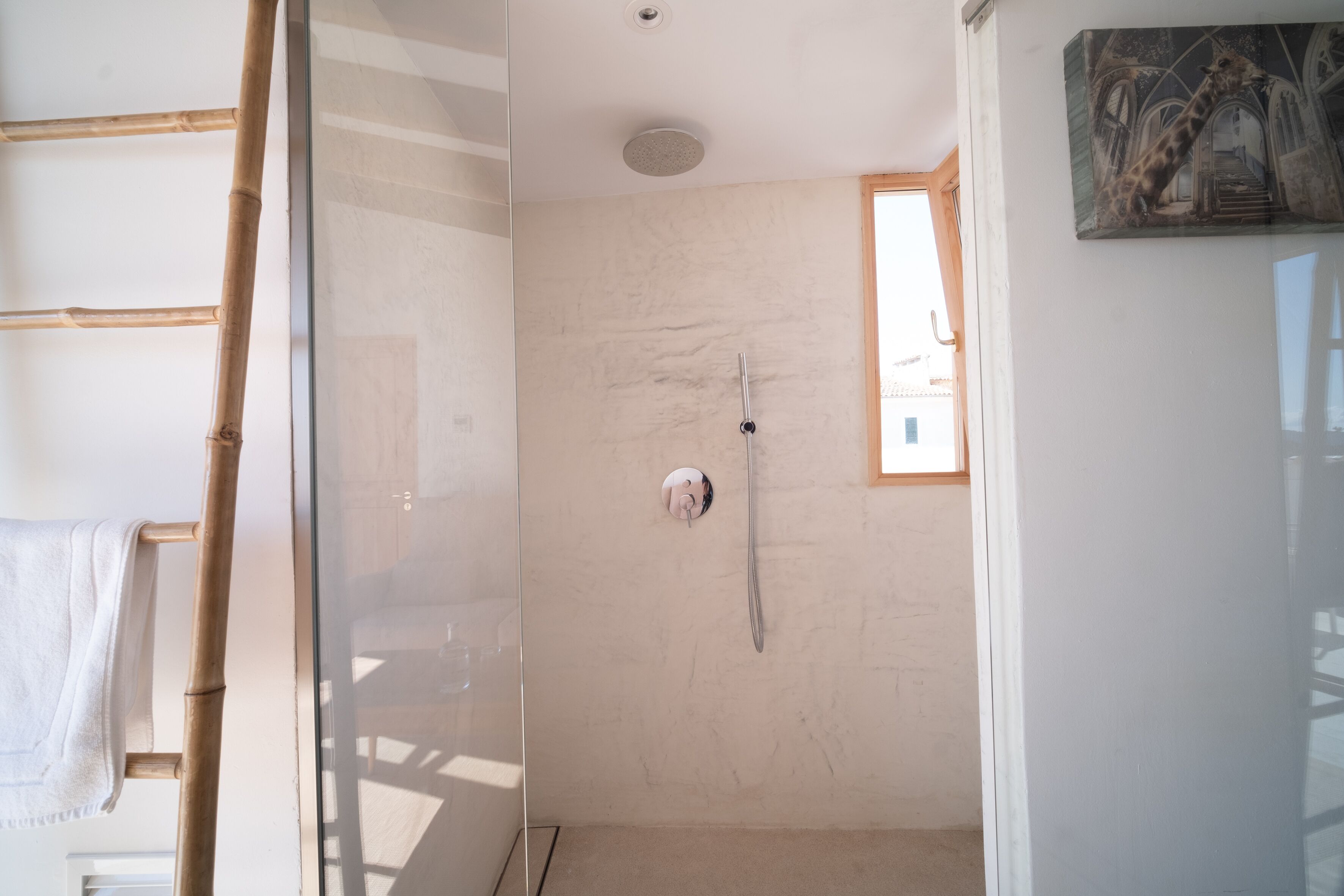 Una habitación con cabina de ducha de vidrio, una escalera de madera y un cuadro en la pared.
