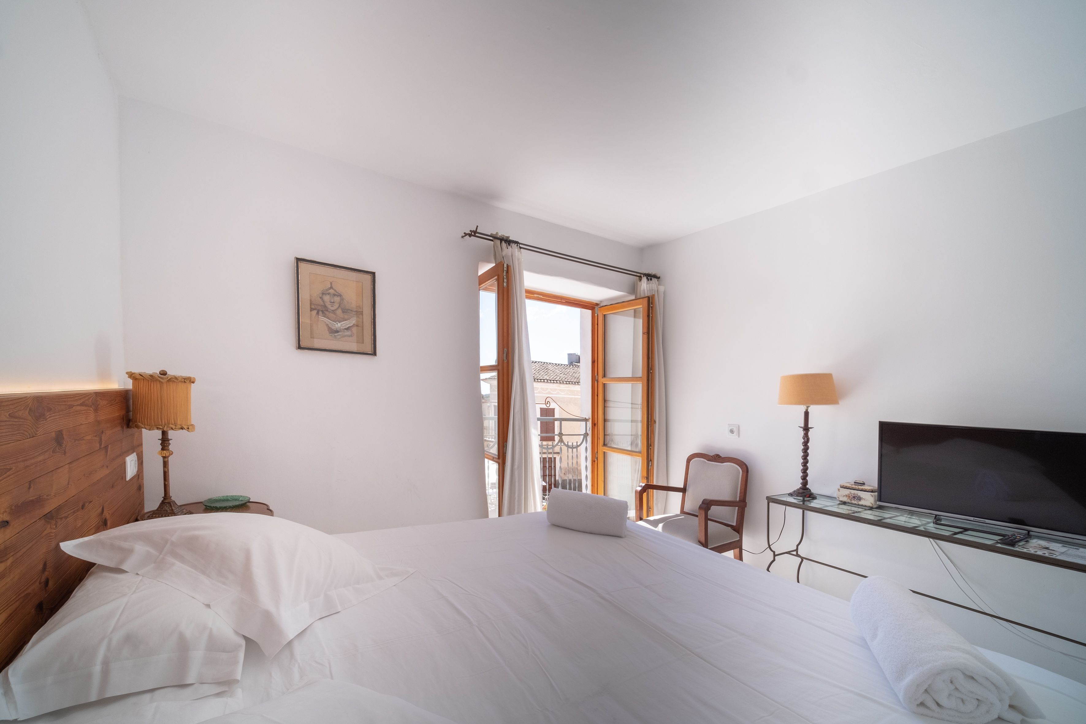 Una habitación de hotel con cama, televisión, silla, lámpara y ventana con cortinas.