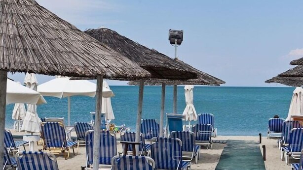 A beach with rows of striped lounge chairs and thatched umbrellas, a green pathway leading to the water, and a clear view of the sea. - Olympic Star (Eretria)