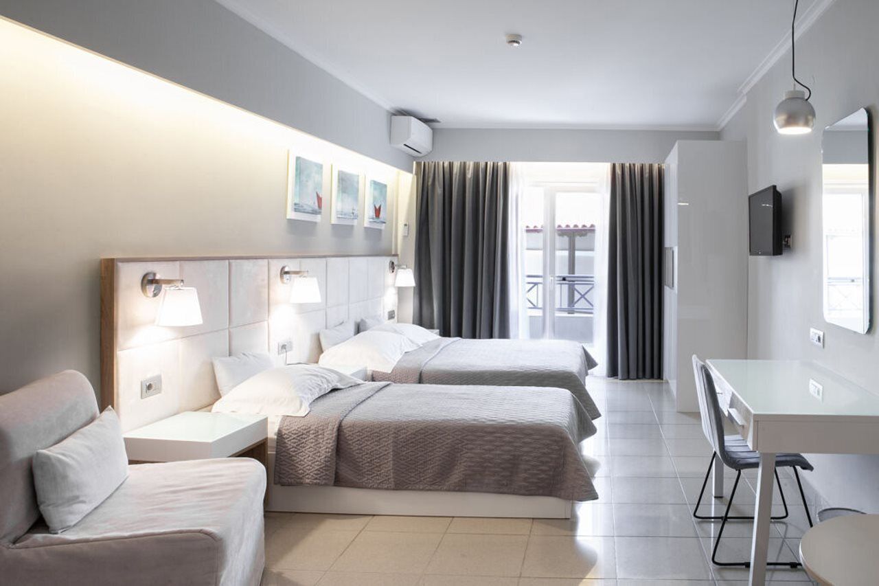 A hotel room with two beds, a desk, a chair, a TV, and a balcony with curtains.
