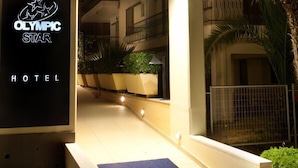 The entrance to the Olympic Star Hotel with a dark blue mat leading to the door, potted plants, and a metal gate. - Olympic Star (Eretria)