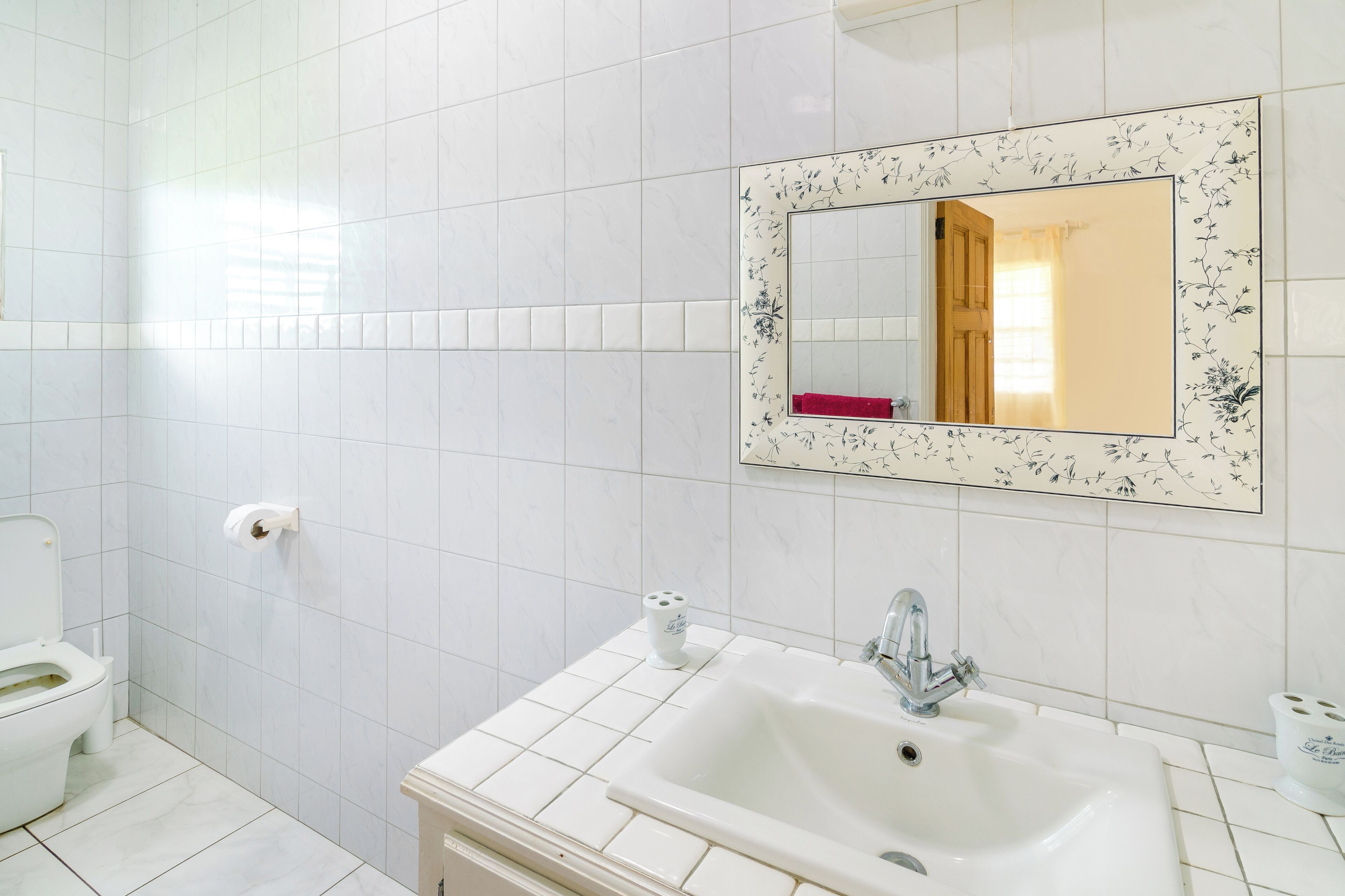 Une salle de bain avec des carreaux blancs, des toilettes, un lavabo avec un miroir et une serviette rouge.