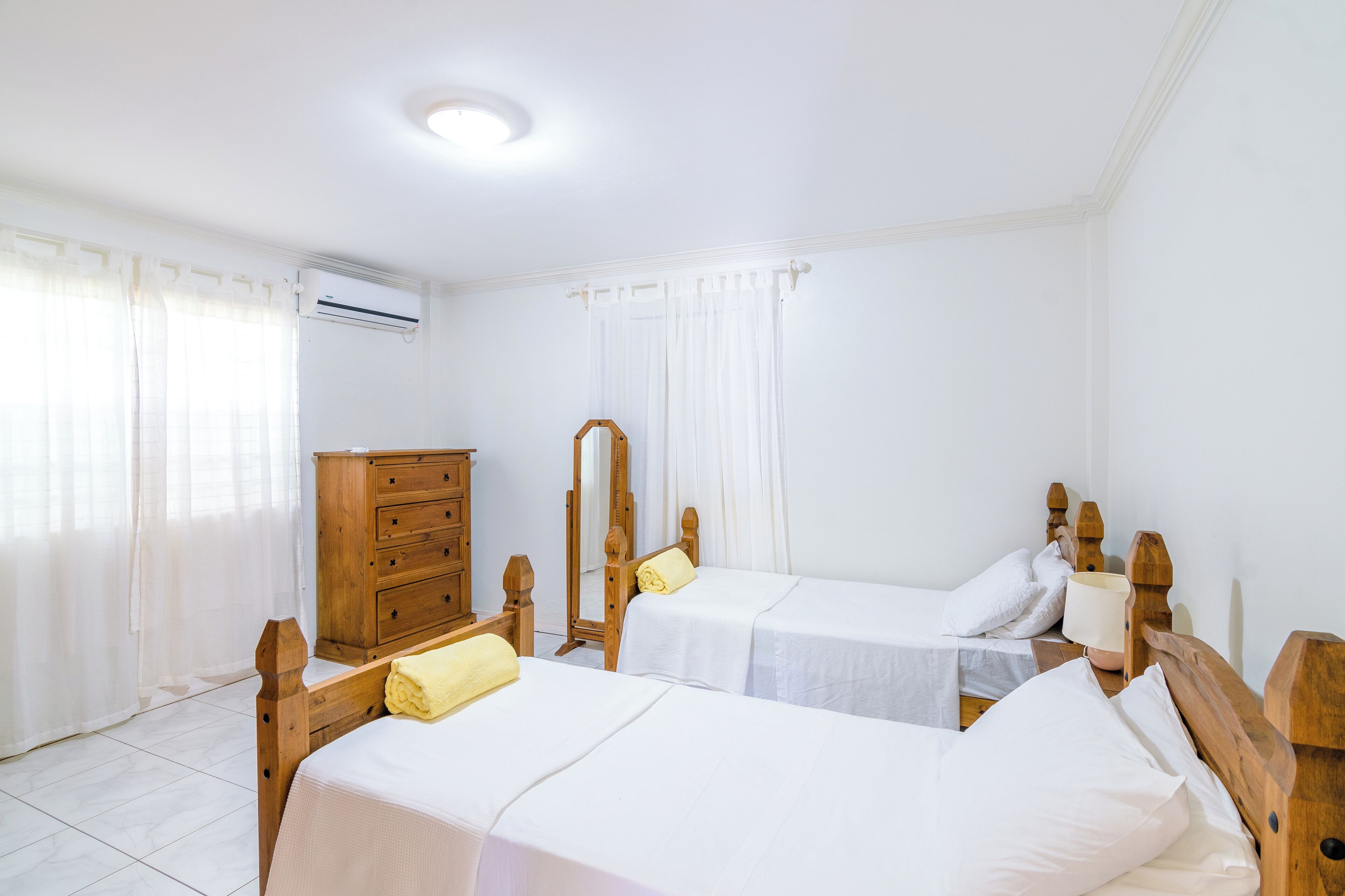 Ein Hotelzimmer mit zwei Holzbetten, einer Kommode aus Holz, einem Spiegel und einer Deckenleuchte.