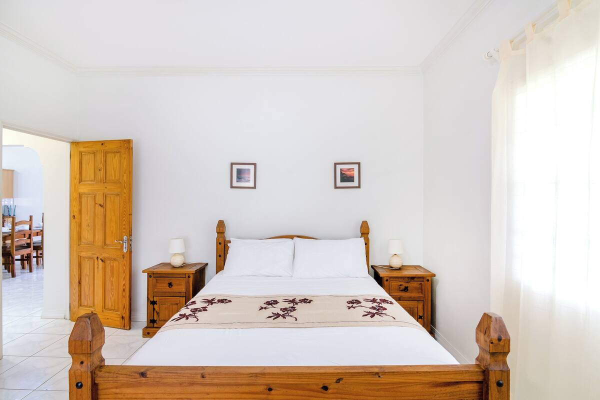 Quarto com cama de madeira, duas mesas de cabeceira, guarda-roupa de madeira e duas molduras na parede.