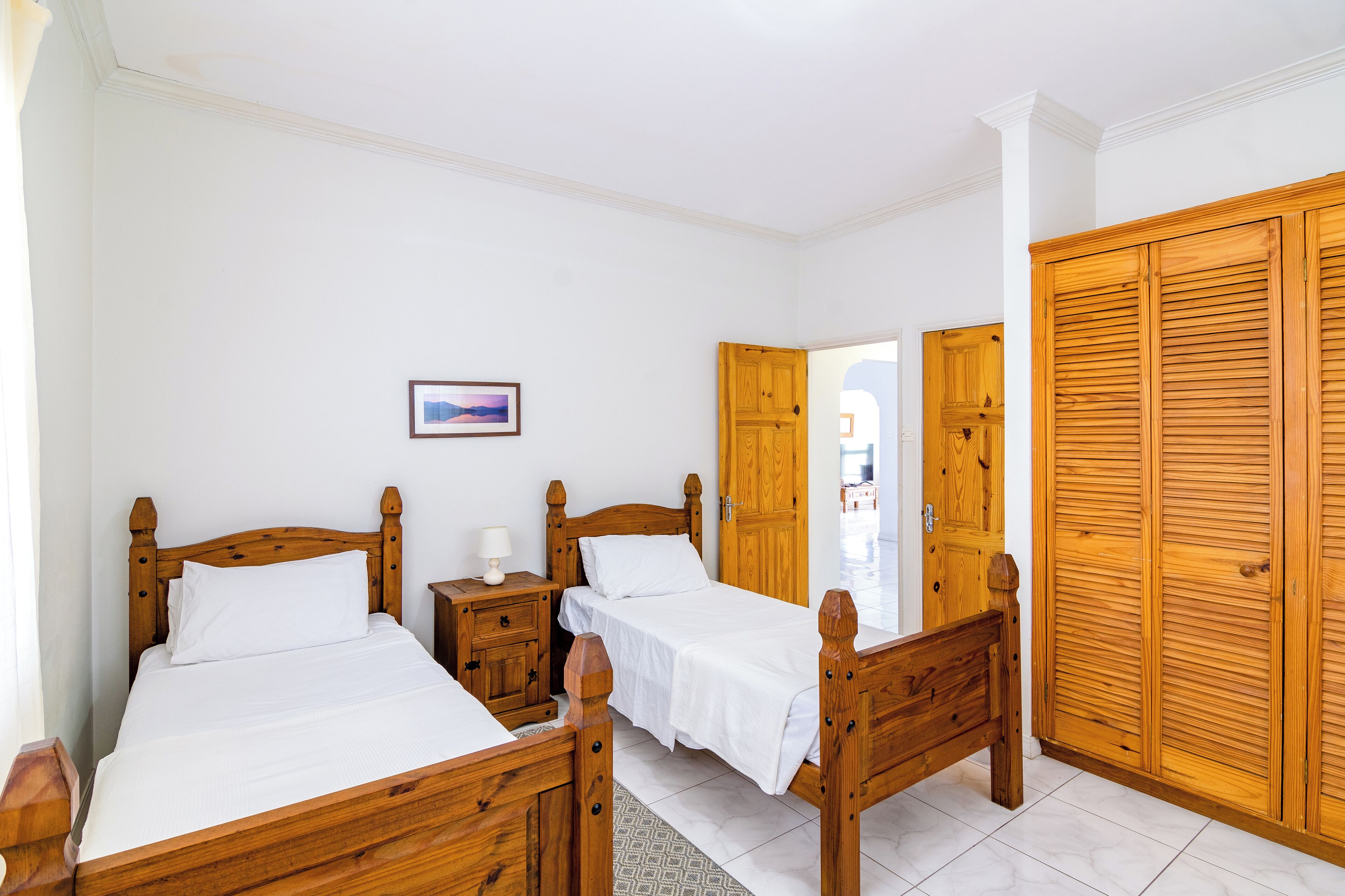 A bedroom with two wooden beds, a nightstand, a wooden wardrobe, and a framed picture on the wall.