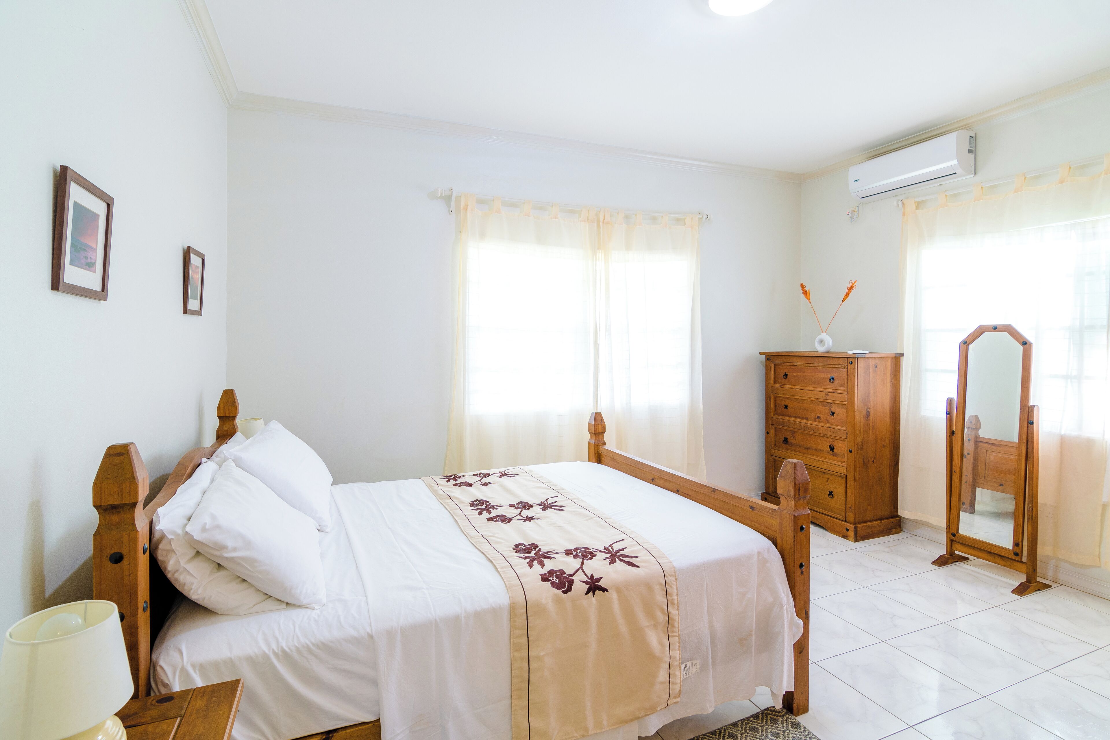 A bedroom with a bed, dresser, mirror, and an air conditioning unit.