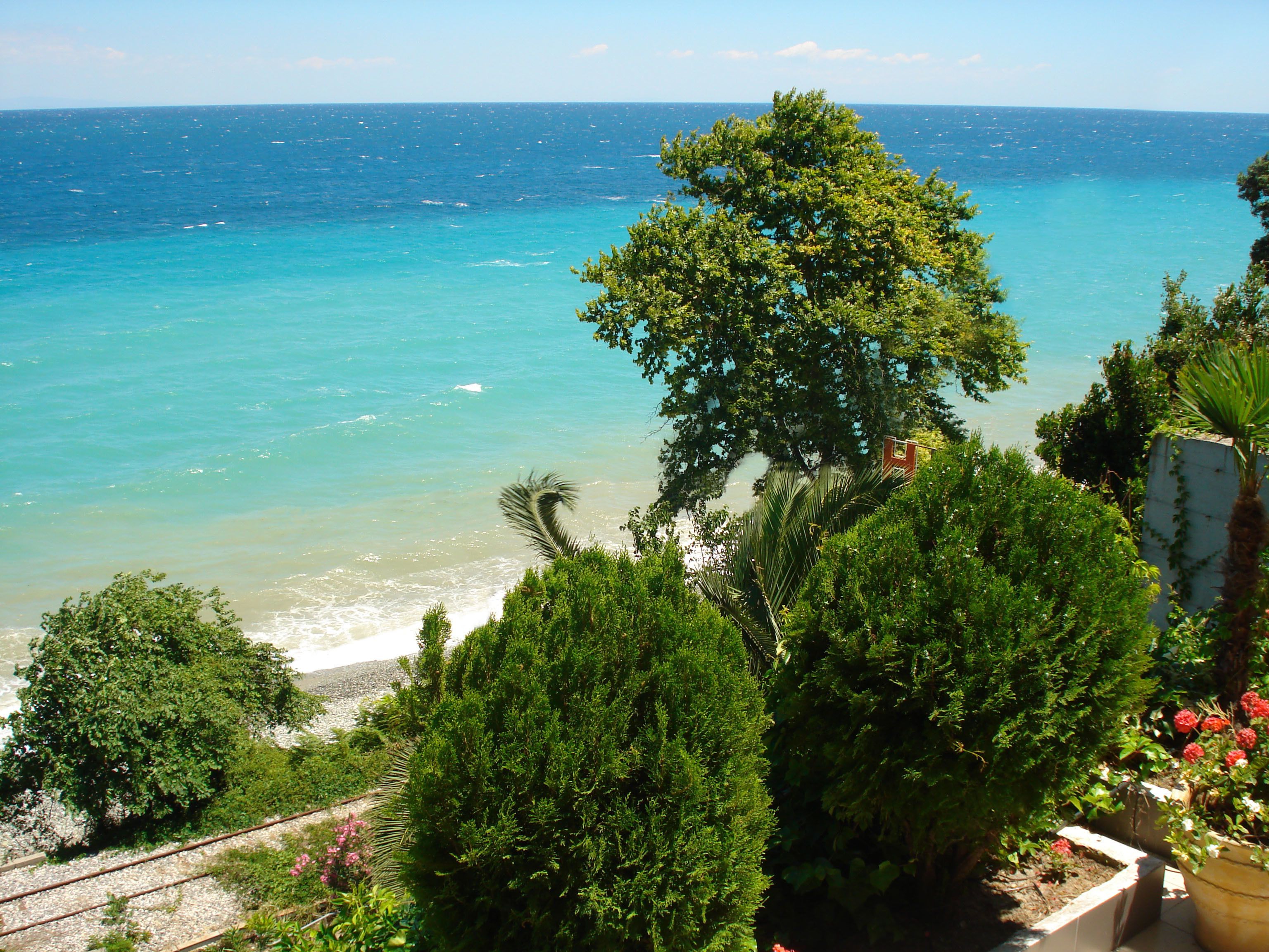 A coastal view with a beach, dense greenery, and a clear blue sea.