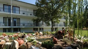 Um edifício com vários andares, varandas, um jardim com pedras e um pequeno lago.