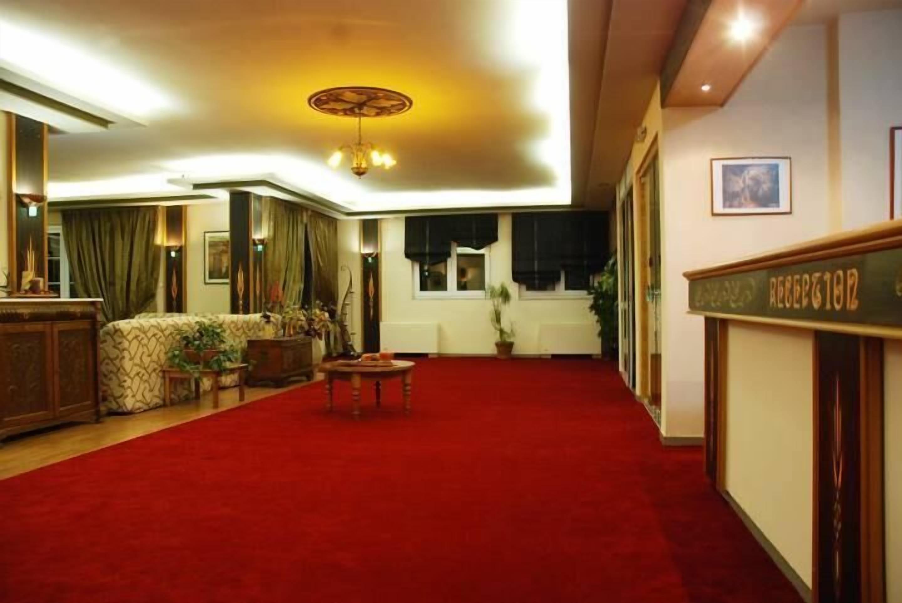 Un hall d’hôtel avec un tapis rouge, un comptoir d’accueil et un espace détente comprenant un canapé et une table.