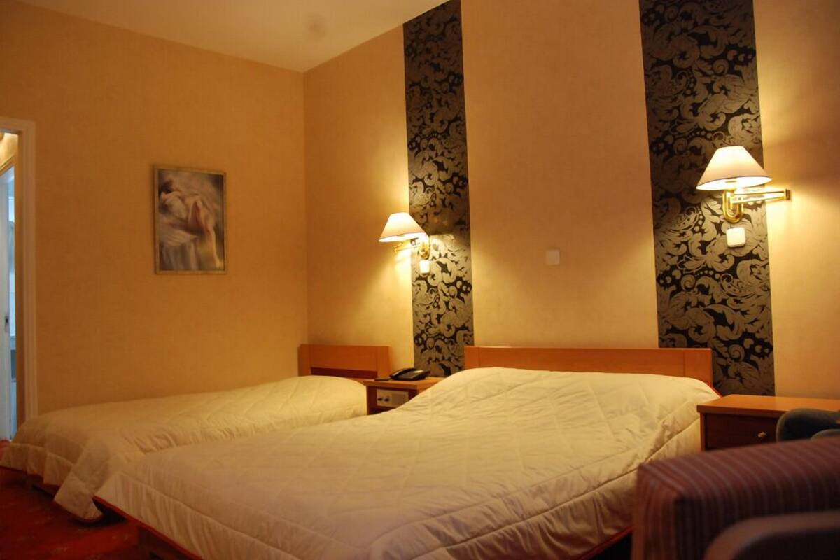 A hotel room with two beds, a nightstand, a lamp, and a floral wallpaper design.