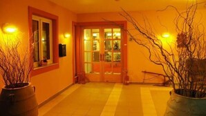 Um corredor com piso de azulejos, porta de madeira com painéis de vidro e duas plantas em vasos.
