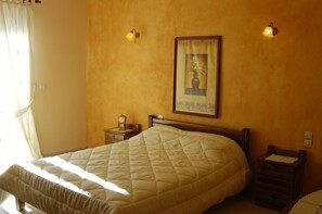 Ein Schlafzimmer mit einem großen Bett, einem Nachttisch mit einer Uhr und einem gerahmten Bild an der Wand.