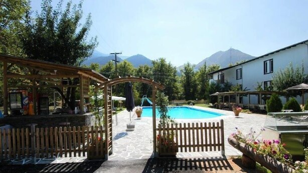 Uma área de piscina com pergolado de madeira, entrada cercada e vista para as montanhas ao fundo.