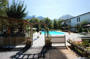 Ein Poolbereich mit einer Hollaube, einem umzäunten Eingang und Blick auf die Berge im Hintergrund.