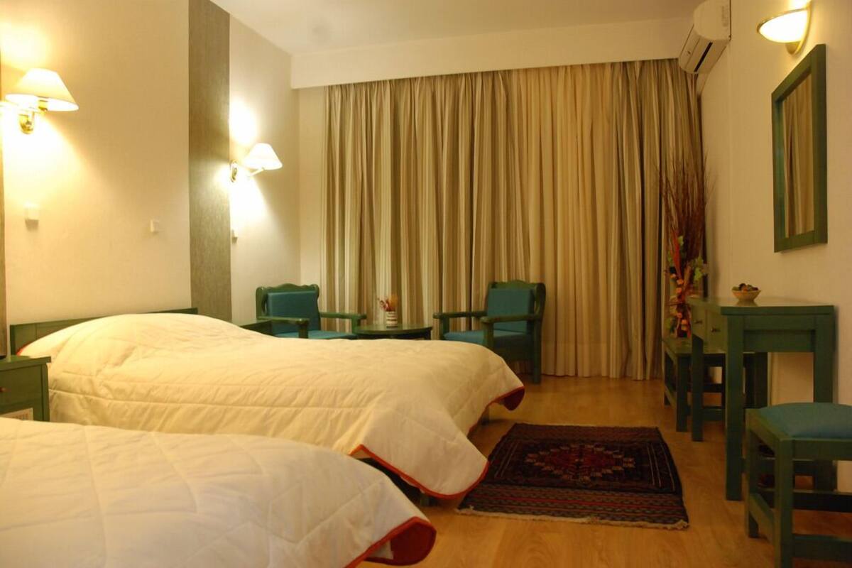 A hotel room with two beds, a desk, two chairs, a small table, a decorative rug, and a curtain.