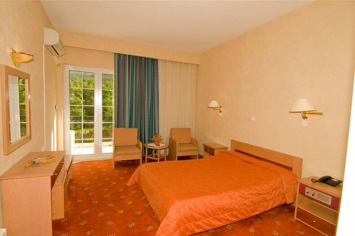 A hotel room with a bed, a desk, a chair, a small table, and a nightstand.