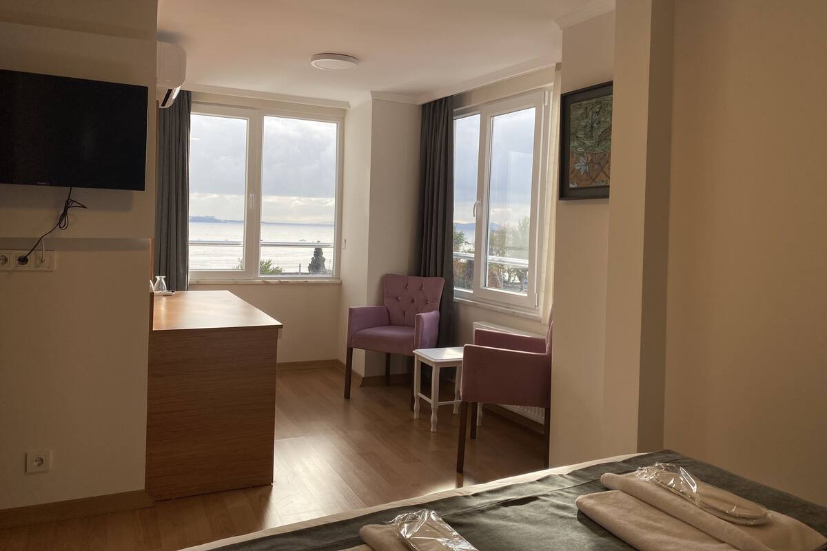 A hotel room with a wooden desk, a purple armchair, a small table, and a bed.
