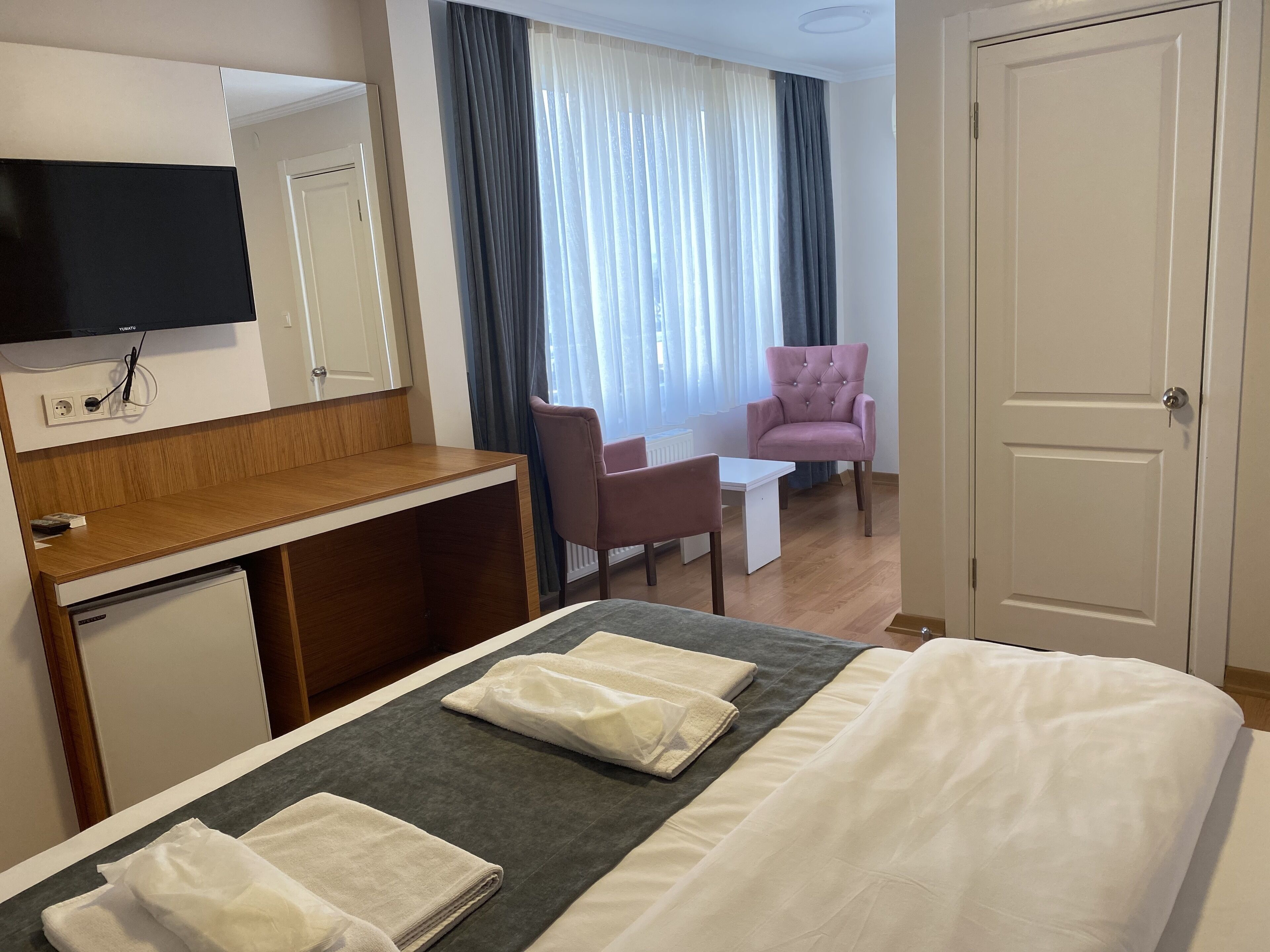 A hotel room with a bed, a desk, a chair, a television, and a door.