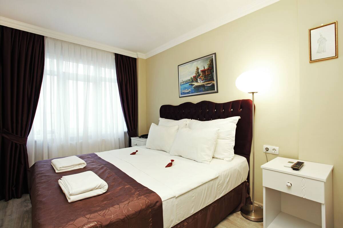 A hotel room with a bed, a nightstand, a lamp, and a painting on the wall.