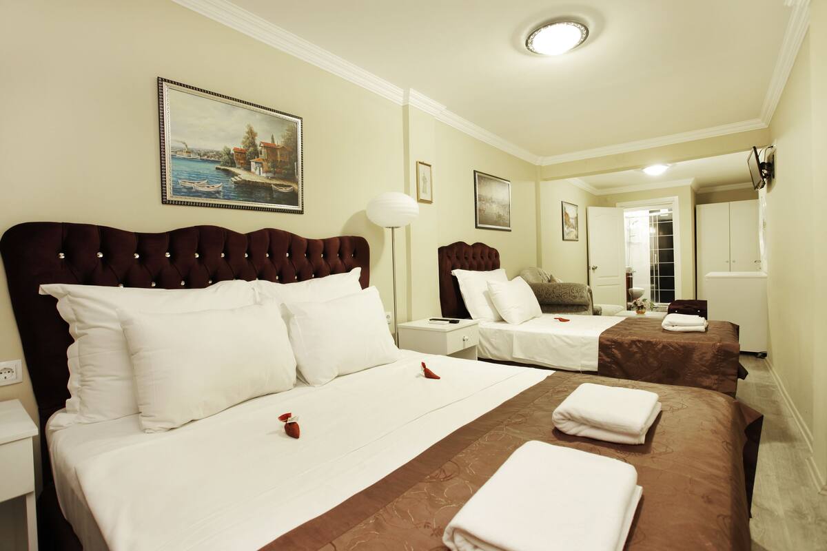 A hotel room with two beds, a large painting, a lamp, and a view of the hallway.