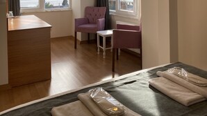 A hotel room with a wooden desk, a purple armchair, a small table, and a bed with neatly folded towels. - Spinel Hotel (Istanbul)